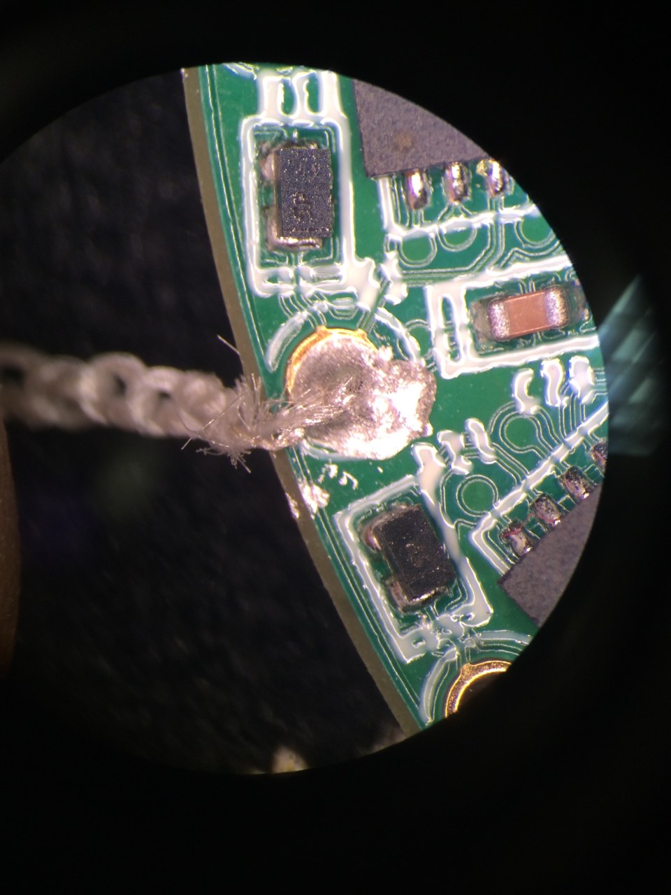 Conductive textile bonded to a PCB pad using conductive epoxy, shown under magnification alongside surface-mount components and circuit traces.