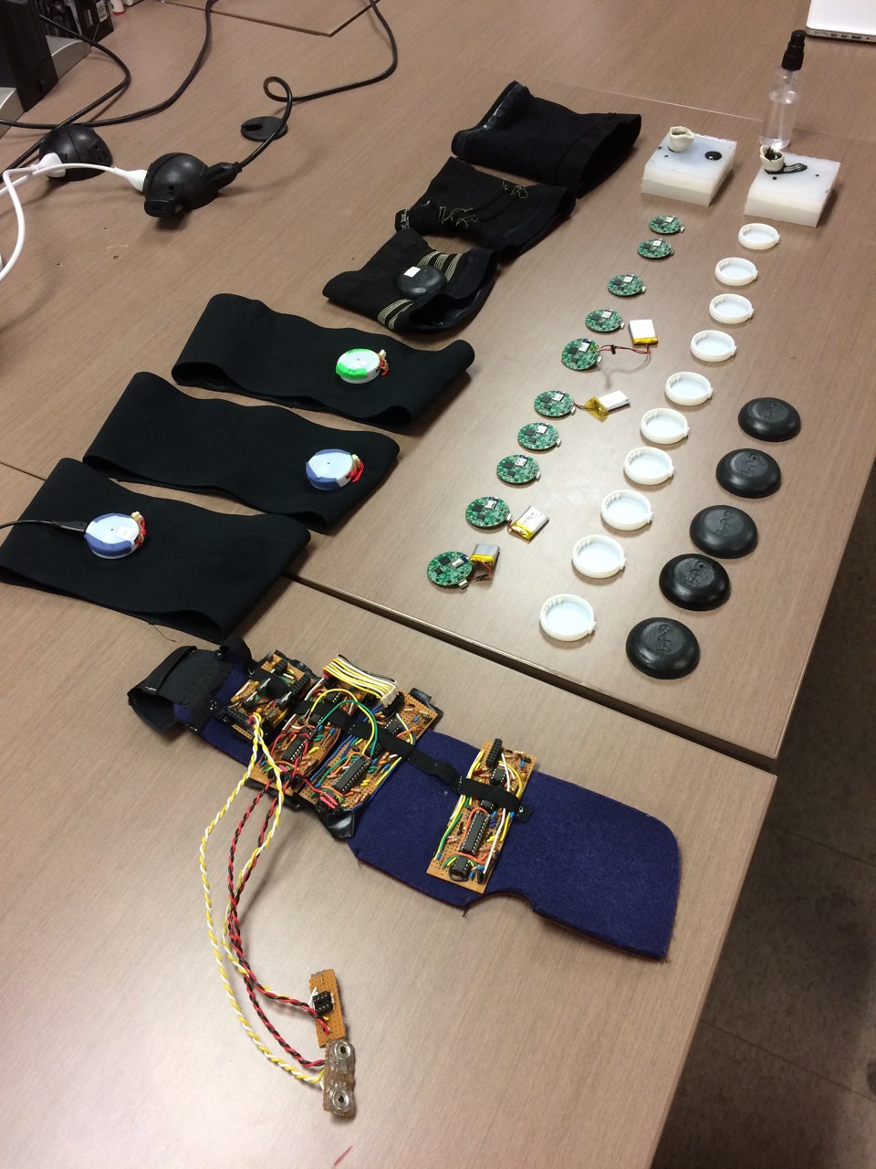 Textile bands, exposed circuit assemblies, circular boards, and enclosure variants arranged together on the workbench.